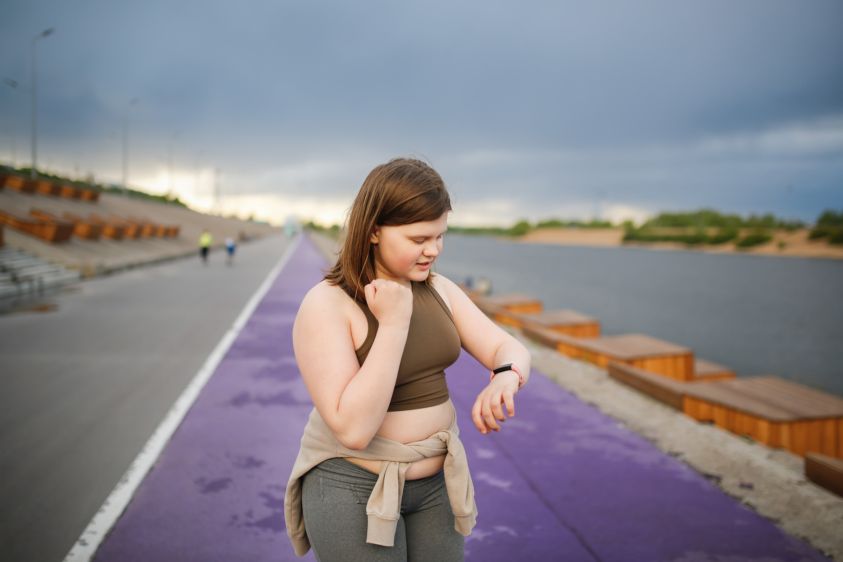 European teenage girl overweight on jog on treadmill along embankment of city, overweight and active lifestyle of teenager